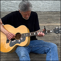 Jonathan Ochshorn playing guitar on pier with water behind